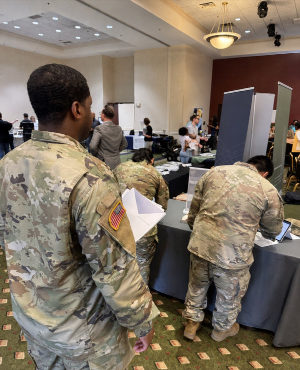 Service members in uniform at a military-to-civilian transition career fair, one holding resume documents